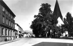 Voss kirke 1939.  Såvidt synlig bak trær. Gate til venstre. 