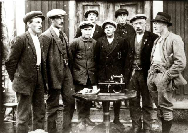 Mannsdrakt, Budalen, Sør-Trøndelag 1920-årene. Gruppe menn samlet rundt bord med grammofon på gårdplass.