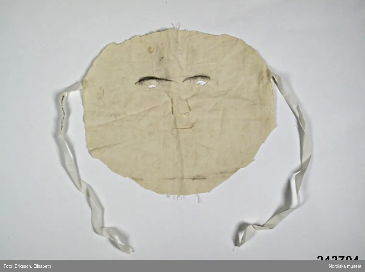 Huvudliggaren:
"Mask, ansiktsmask av vitt bomullstyg med knytband.
Nygjord 1951. Ingår i utklädsel av Valborre."
Se även 242.700-242.707