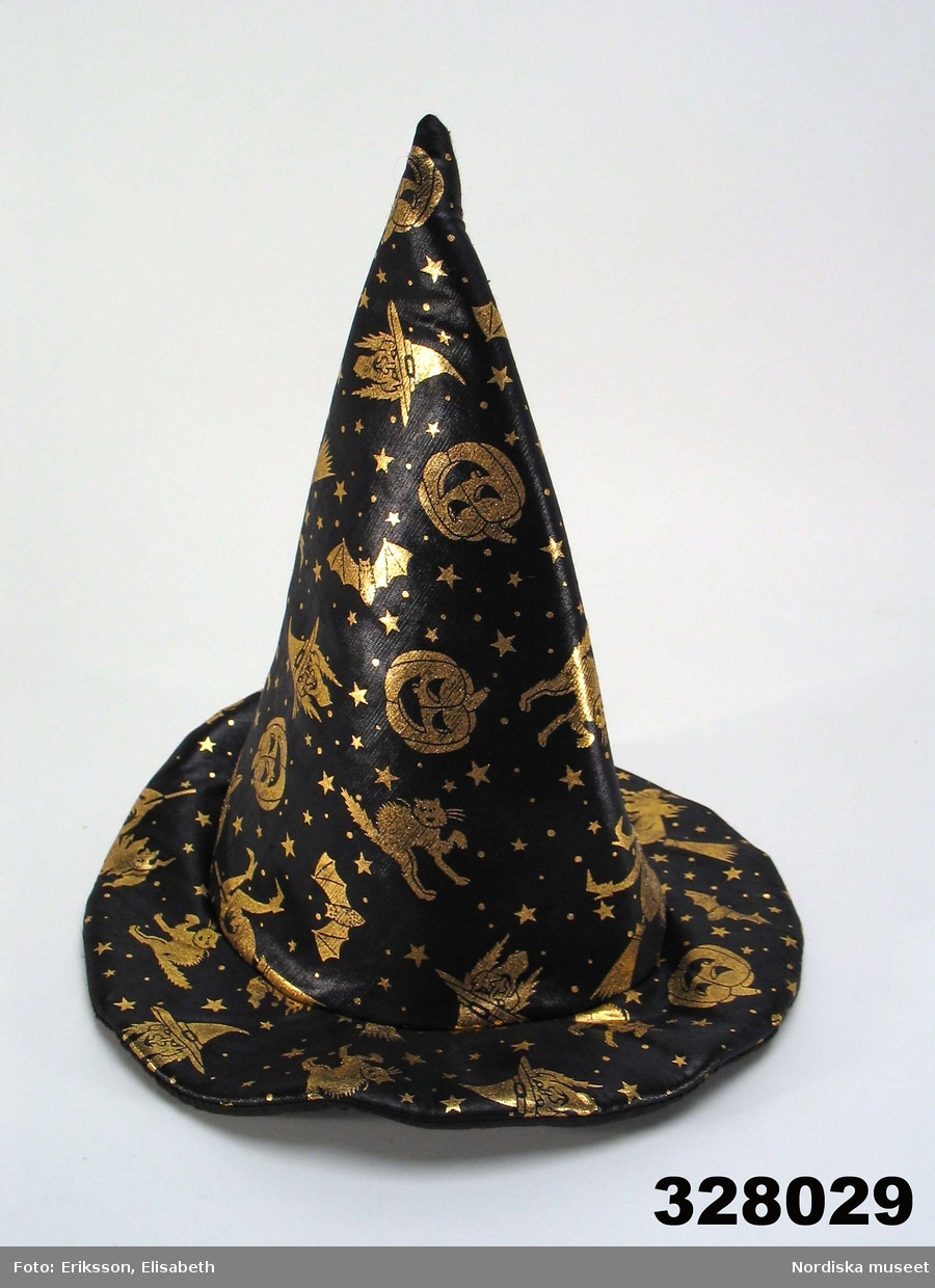 Huvudliggaren:
"Häxhatt, halloweenutklädsel. Konformad, svart polyester m guldtryck, mönster strödda häxor, pumpor, stjärnor m.m., brätte 7 cm, foder svart bomullstyg, styvt mellanlägg. Inköpt på Buttericks ca 2000. Anv Klara Höök (f 1992) bl.a. vid halloweenfirande i Sthlm 2002. H 35 cm B 34 cm. I[nköpt] 14/11 2002 från Klara Höök Klara Norra Kyrkogata 20 Stockholm. [...]"