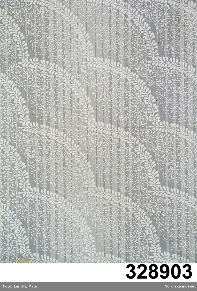 Tapetprov. Mönstret "Snö i stigande bågar" trycktes av Zuber i åtta färgställningar 1828. Ljusgrå fond med en lätt randning i något mörkare grått, över dessa ränder faller vita flingor, halvt genomsiktliga och av olika lätthet, från diagonalställda båglinjer. Bågarna formade som tunna stänglar med parvisa blad men de är också symbol för snömolnen. Mönstret ritat av Henri Küpfer, chefsdessinatör vid fabriken 1825-30 och beskrivs i fabriken Zubers liggare som "dessin à la neige à picottage en arcs montants obliqment" (snö med prickar i stigande bågar på snedden). Grått blev en modefärg på 1820-talet. Till grå tapeter användes ofta bårder i lysande färg.
Tapeten hade ursprungligen inv.nr. 108.600:3.
/Maria Maxén, november 2006.

Ingår i en samling tapeter med olika mönster, alla tidigare inmärkta under inv.nr 108.600:1-49. I samband med inventering och flyttning av tapetsamlingen 2006 tilldelades de olika mönstren nya inv.nr (328.901-328.948, se även 241.333) och endast själva pärmen fick behålla inv.nr 108.600
/Ingrid Frankow 2006-07-12

Huvudliggaren (från dess ursprungliga inv.nr 108.600):
"1-48 48 tapetprover komna från Tengbergska huset i Göteborg."

Bilaga: (från dess ursprungliga inv.nr 108.600):
Korrespondens ang tapeterna och Tengbergska huset.

Katalogkort: (från dess ursprungliga inv.nr 108.600)
"Tapetprover
(Text gällande hela samlingen)
Tapetprov och bårder från det Tengbergska huset i Göteborg. Alla ytmönster är handtryck med limfärg på ett tunt jämnt papper i sammanklistrade ark. De flesta har svagt satinerad yta. Vådbredden är oftast 50 cm och mönstrets bredd ca 47 cm. Flera är i den på 1820-talet moderna gråskalan, medan andra är i lysande färger. Bårderna är tryckta på något tjockare papper och av olika bredd. De flesta har velourtryck i en färg, inte sällan med övertryck i limfärg som då får en extra lyskraft."

Katalogkort:
"Tapet, handtryck, papper. Motsvarande prov i Le Musée du Papier peint, Rixheim, inv.nr. 20 2494 b. 'Fabricant: Jean Zuber, Rixheim 1828. Fond gris clair. Impression foncé de fond, blanc. 0,470x0,650" samt äldre beskrivning, trol. tillverkn. journal: "2494 dessin à la neige à picottage en ares mont.ts obliqant, ancien 2304 de Küpfer
fd bleu clair   fd gris clair
"  lila                 citron
"  olive              pierre
"  pistache         
"  vigogne'.
Uppgifter från M. Bernerd Jacqué, Tapetmuseet Rixheim 18/4 -2000.
Se brevboken 50:571/00-572/00.
/EHK [Elisabet Hidemark]

På nästan alla finns anteckningar på baksidan på franska, några är stämplade med "Déposé J Z Cie" inom en oval (Jean Zuber & Cie, Rixheim, Frankrike), men även andra fabriker är representerade.
Det Tengbergska huset var ett 1700-talshus vid kanalen i centrala Göteborg som i flera generationer ägts av samma släkt, först av färgeridirektören Isac Tengberg (1775-1842). Den samling tapetprover som funnits i huset var förmodligen importerad av Tengberg för att säljas i Göteborg. Av en släkting till familjen Tengberg mottog Nordiska museet tapetsamlingen inför rivningen av det Tengbergska huset 1907.
/Maria Maxén, febr. 2006.

