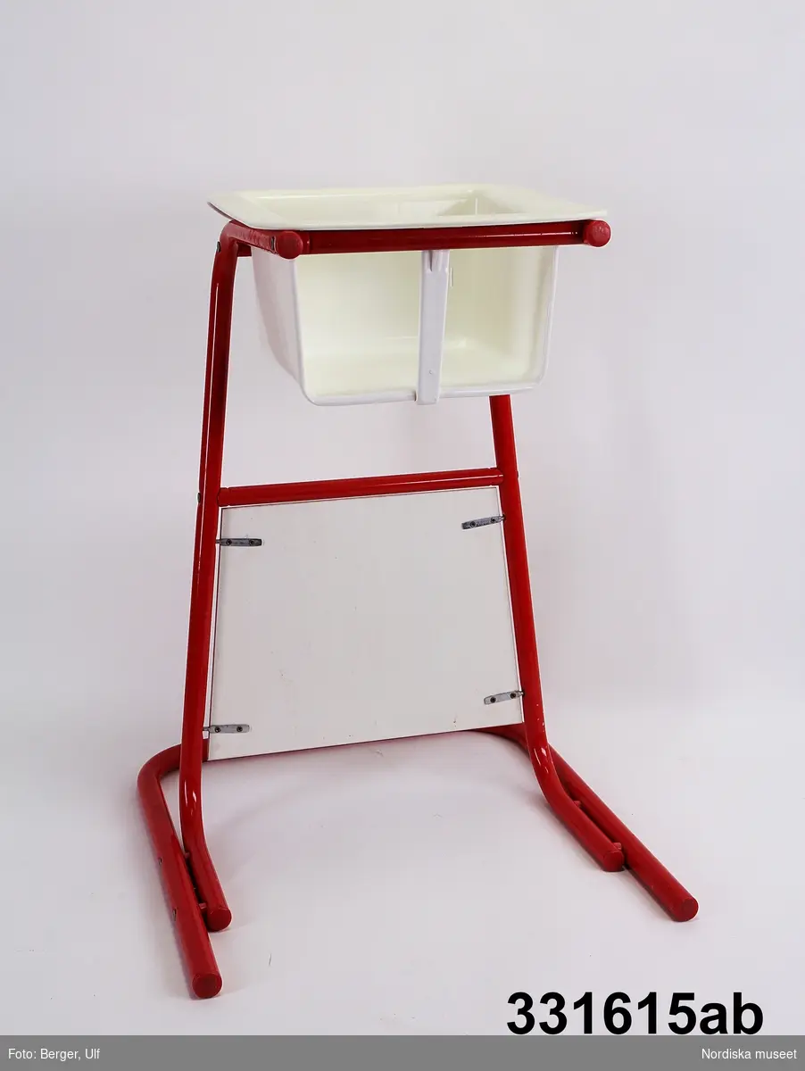 Barnstol:
a) Löstagbar sits av vit propenplast. små plastspärrar som går att trycka in så sittsen går att plocka bort.
b) benställningrött epoxilackerat stålrörsstativ, bord av lackerad träfiberplatta. 

Möbeln går att använda på två sätt: stående vid matbordet eller liggande med bordsskivan uppåt, varvid barnet får en egen arbetsplats för pyssel och lek.
/Karin Dern 2012-10-10