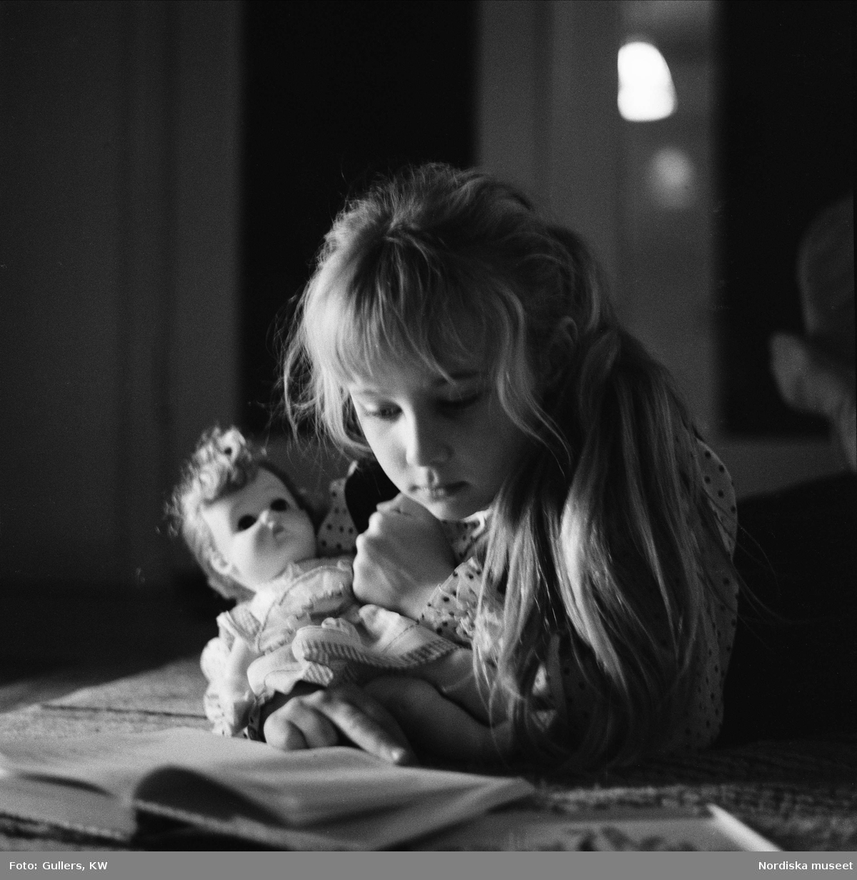Flicka läser bok med docka i famnen.