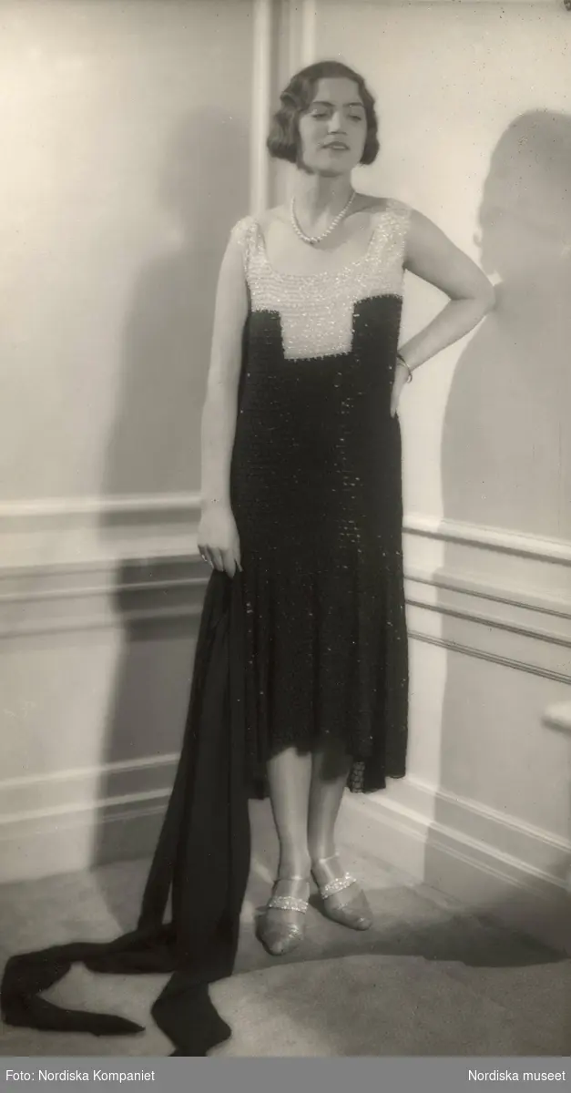 Mannekäng i salongen på NK:s Franska damskrädderi klädd i originalmodell uppsydd hos Coco Chanel i Paris. Svart och vit klänning med pärlor. I handen håller hon en svart sjal.