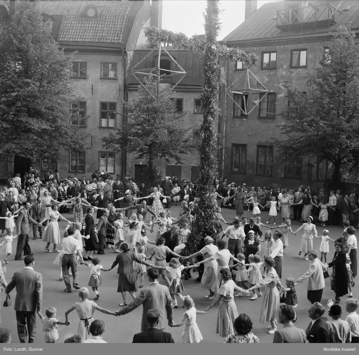 Årshögtider. Midsommar. Midsommar i Gamla stan, Stockholm. Människor dansar runt en midsommarstång på en innergård. 