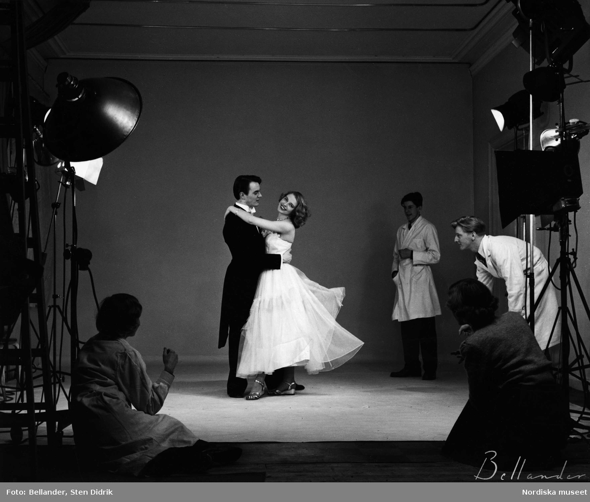 Modefotografering i studion. Ett par dansar omgivna av studiolampor och assistenter.