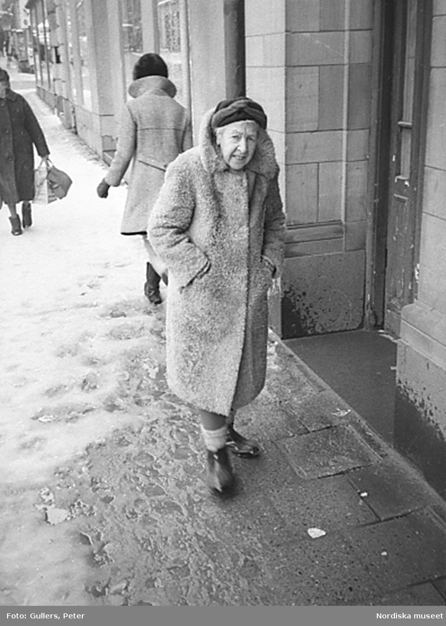Äldre kvinna i kappa på snöslaskig gata, Stockholm
