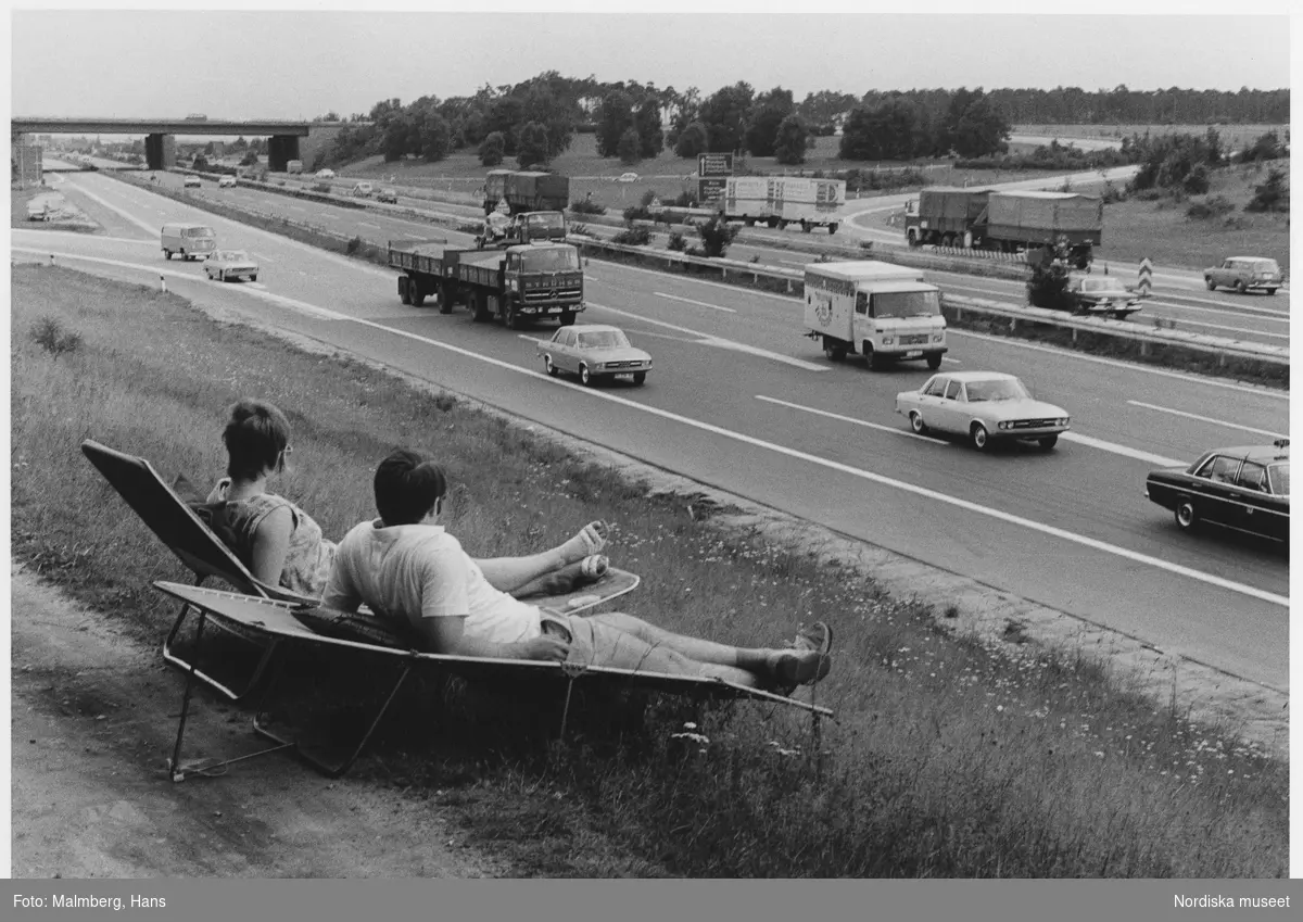 Autobahn, Västtyskland, 1972. Ett par i solstolar tittar på motorvägstrafik.