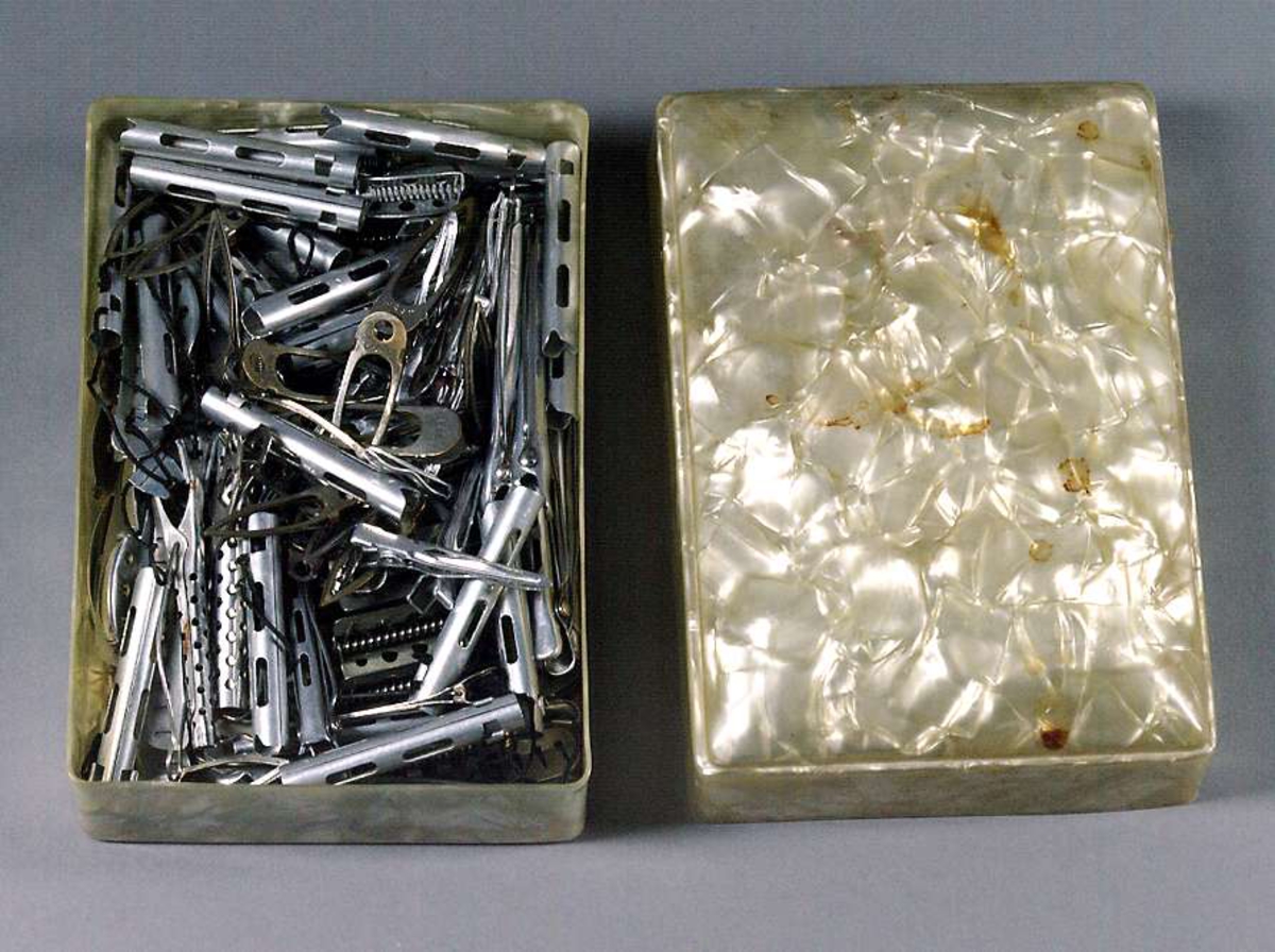 En stor samling hårklämmor och hårrullar av metall i olika utförande. Förvaras i en ljusgrön plastask med lock (UM30602b).