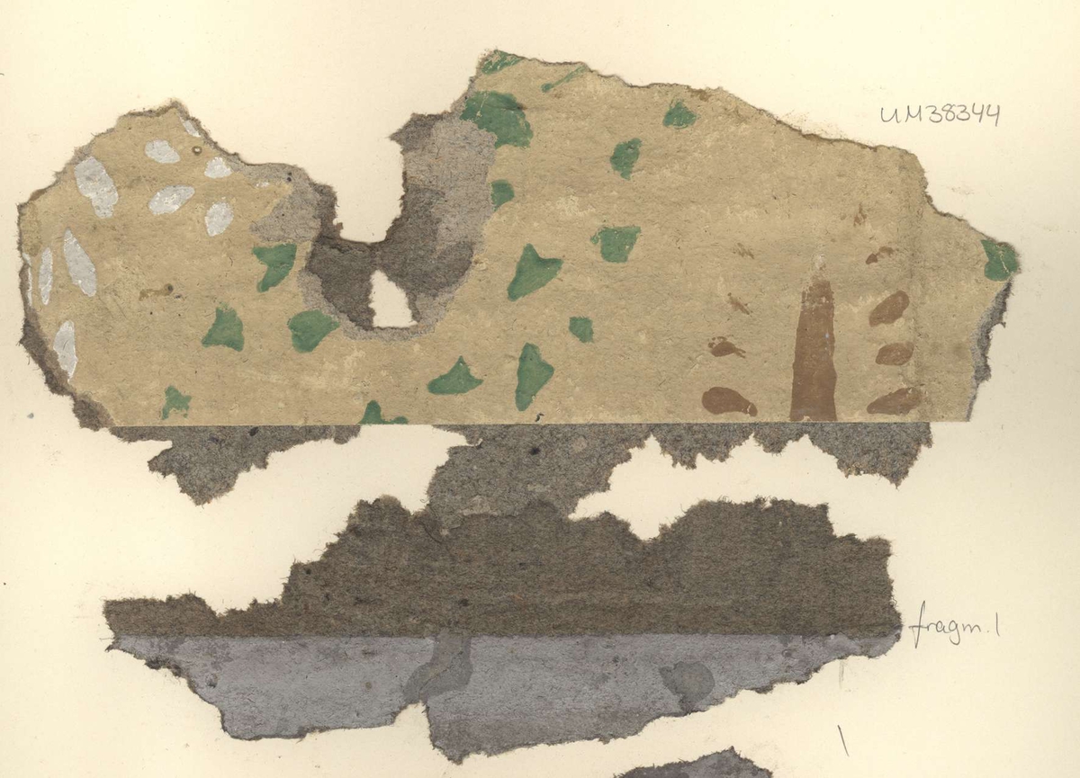 Fragment av tapet av papper, schablonmålad, beige bottenfärg med mönster i grönt, vitt och brunt. Fragmentet märkt med siffran 1.
