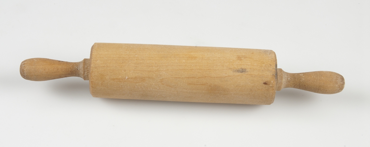 En bakkavel bestående av en genomborrad cylinder av trä som rullar fritt kring en axel av metall. Axeln är försedd med handtag av trä i ändarna.