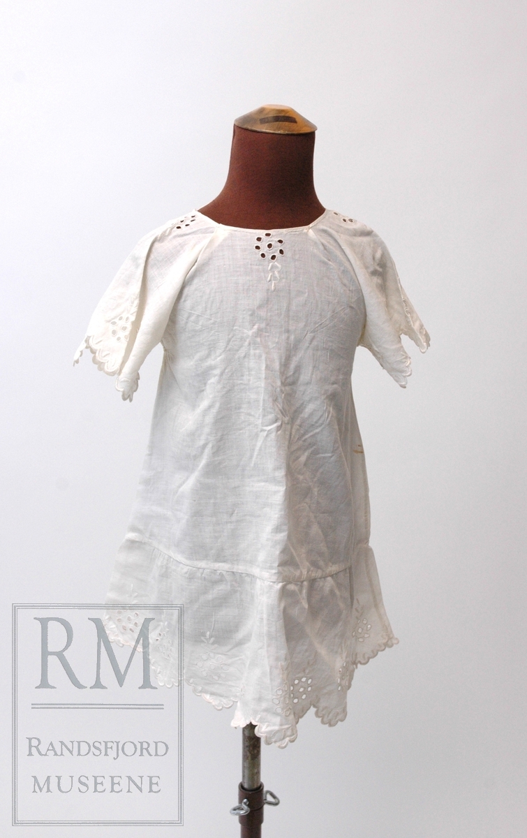 Kjole og lue til jentebarn (1-2 år). Kjole og tilhørende kappehue i hvitt bomullstoff (cambric) med engelsk (hull)broderi. Tidlig 1900.