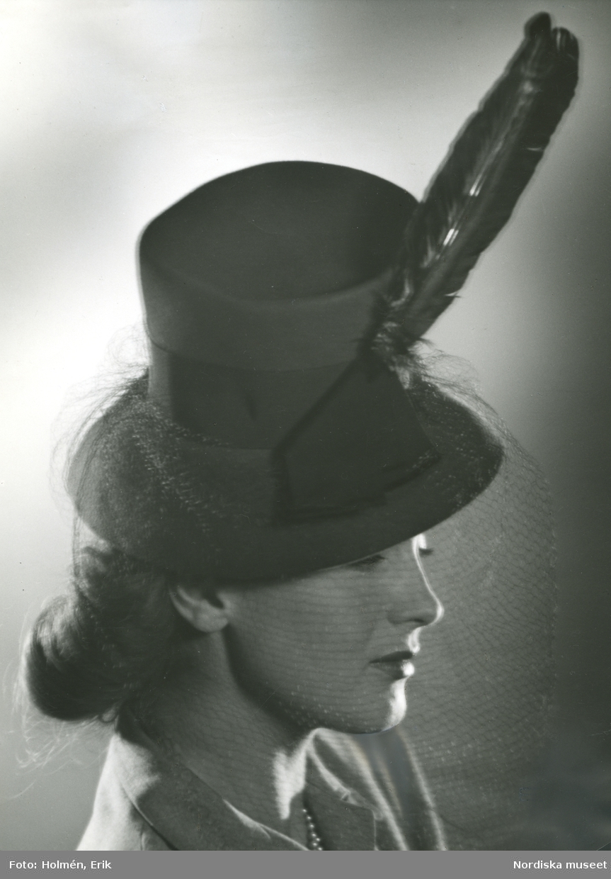 Porträtt av mannekängen och skådespelerskan Hjördis Genberg i hatt med fjäder, flor och hattband, från Madame Suzy.