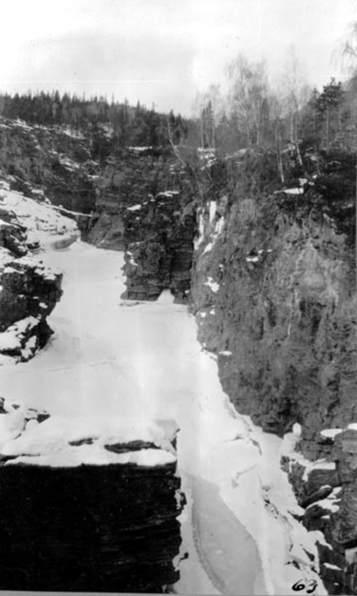 Harpefossen i Gudbrandsdalslågen, i Sør-Fron kommune i Oppland fylke, fotografert fra vegbrua over fossen en vinterdag i 1909 eller 1909.  Vi ser ned på et islagt og snødekt elveleie, som i perioder med stor vannføring i sommerhalvåret var både stridt og mektig, inntil fossen ble regulert i 1960-åra. 

Før Harpefossen ble utbygd i 1960-åra var det et fall på cirka 25 meter over en strekning på om lag en kilometer her.  Fossen startet med et stup i elveleiet like ved garden Solbrå.  Nedenfor smalnet elveløpet i ei bergkløft med strid strøm og nesten loddrette vegger.  «Elveleiet i fossen er saa trangt, at vandet under flom hvirvles op langs de bratte fjeldvægge; der er store jettegryder», forteller geologen og topografen Amund Helland i sin beskrivelse av vassdraget (1913).  Det er innlysende at tømmerfløting i et slikt elveleie var både besværlig og farlig.  Helland framstilte det slik: «Laagens bredde er i Harpefoss 15-20 m.  Fossen er ofte besværlig for tømmerflødningen.  Naar der er lidet vand, bindes tømmeret let.  Under høivand gaar flødningen noksaa godt. »