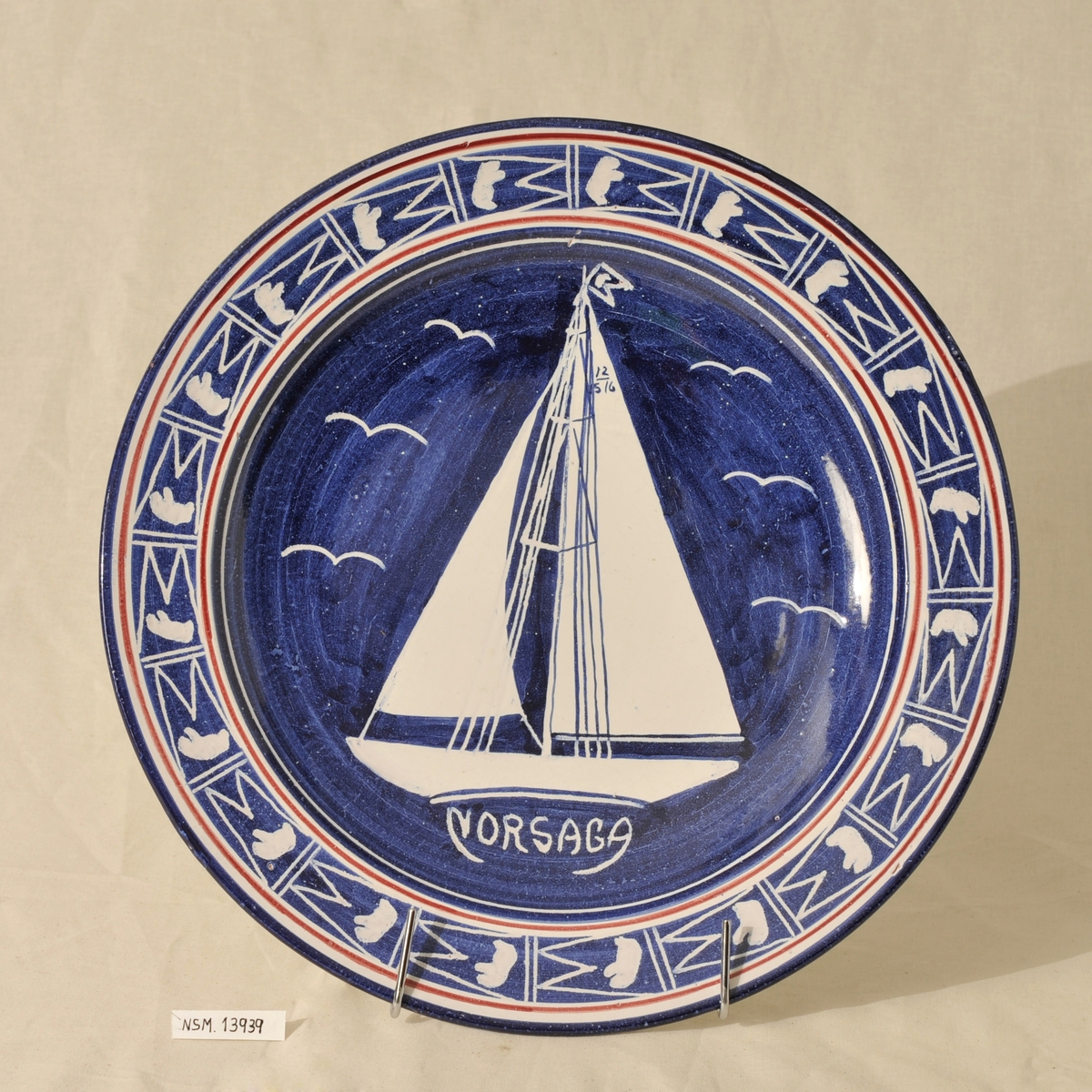 Keramikkfat med tegning av seilbåten Norsaga som har tilhørt Charles Ulrik Bay. Blått fat med hvit dekor.