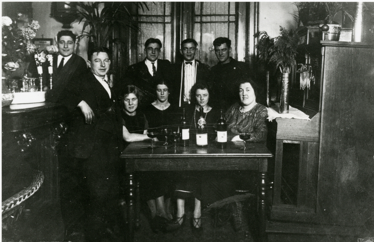 Fem stående menn og fire sittende kvinner med vin, i gresk kafe i Antwerpen, 1922.
