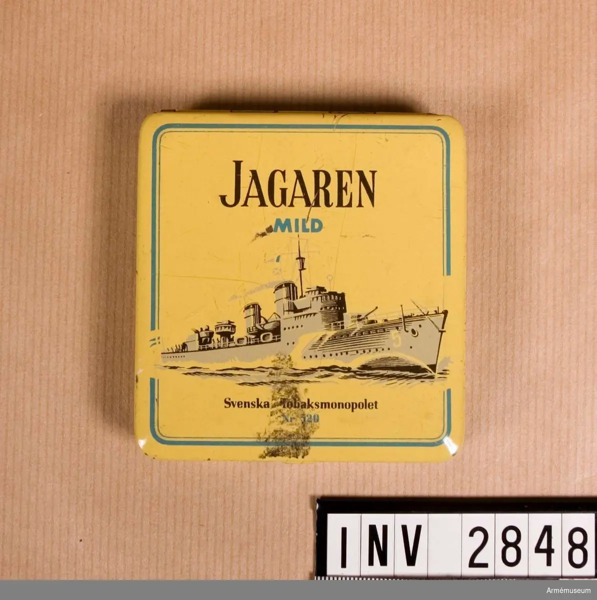 Ask med uppfällbart lock, använd till så kallad piptobak. På locket står "JAGAREN" och under "MILD" samt bild av en jagare i full gång. Under fartyget står "Svenska Tobaksmonopolet nr 520".