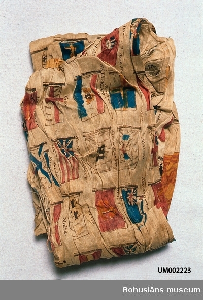 Silketyg med tryckt mönster av olika flaggor (nations-, stads- och handelsföretagsflaggor mm?). Färgerna är nu beige botten och tryck i mörkbrunt, blått, blåtonat rött, gråtonat gult. På ett ställe texten: "Greek: 1829". Datering gjord efter det.
Bredvid duken ligger två etiketter: "Duk med flaggor Gåva av Simmersröd Barnhus U (?) Överstelöjt Hjortsberg" och " Gåfva af Skräddaremästare Gylb... (oläsligt) i Resteröd 1880". Årtalet 1880 är möljligen det år då Simmersröd Barnhus fått duken.
I mycket dåligt skick. Bitvis helt söndertrasad. Troligen färgförändrad. Går ej att lägga ut för mätning, trasas då sönder.

Ur handskrivna katalogen 1957-1958:
Sidenduk m. flaggor
Mått: 85 x c:a 65 cm.
vitt (?) siden m. flaggor i färgtryck. Mycket trasig. Simmersröd, Ljungskile.