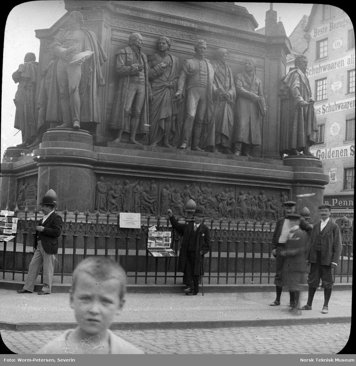 En gutt i forgrunnen og noen menn står foran et monument av Friedrich Wilhelm III i Køln.