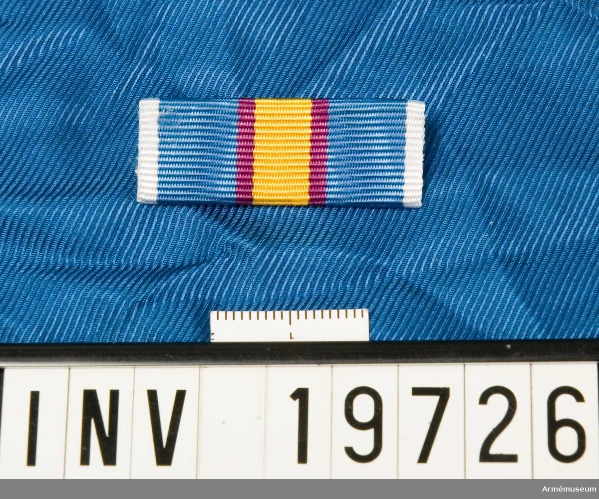 Blått band med vita kanter och en bred gul rand i mitten åtföljd av en purpurröd rand på vardera sidan. Förvaras i en ask tillsammans med en medalj och en miniatyrmedalj.