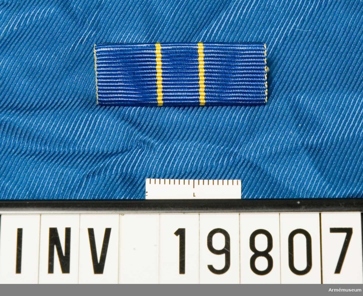 För 6 fördelningen. Blått band med två gula streck mot mitten. Släpspännet förvaras i ask tillsammans med en medalj.