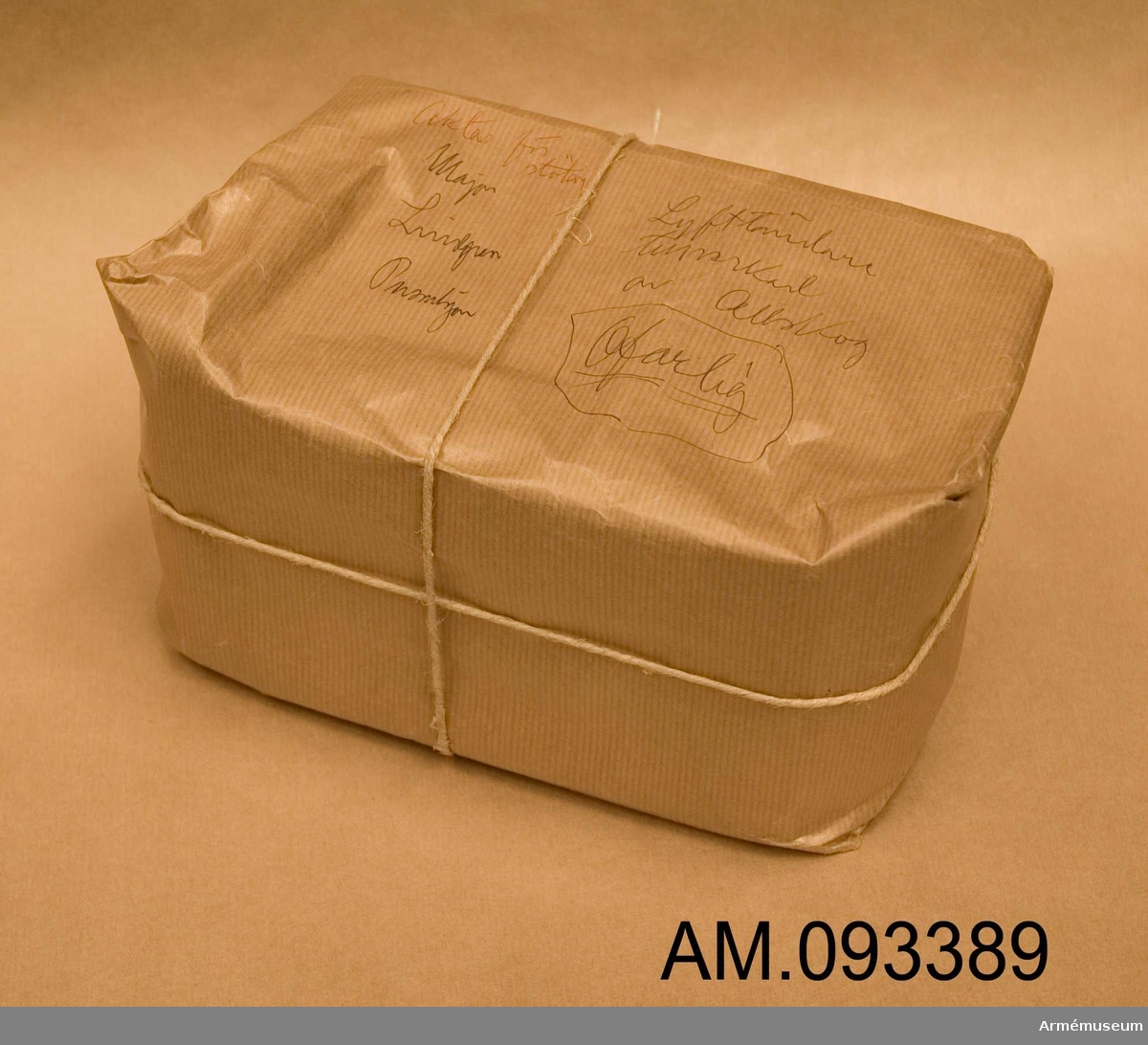 Paket i brun wellpapp med brunt snöre. Har sannolikt använts för att testa om det går att smuggla in ett paket som skulle kunna innehålla en bomb på svenska myndigheter. Innehåller äldre ofaliga elektriska komponenter för att efterlikna en verklig sådan från tiden efter andra världskriget. En av kartongerna har en märkning från augusti 1947.
