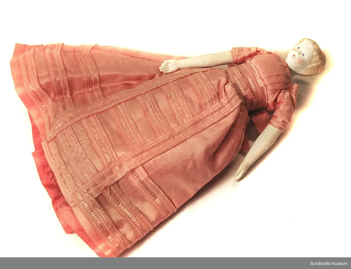 Flickdocka med huvud, hår, armar och ben av biskviporslin. Klädd i lång klänning av rosa siden.