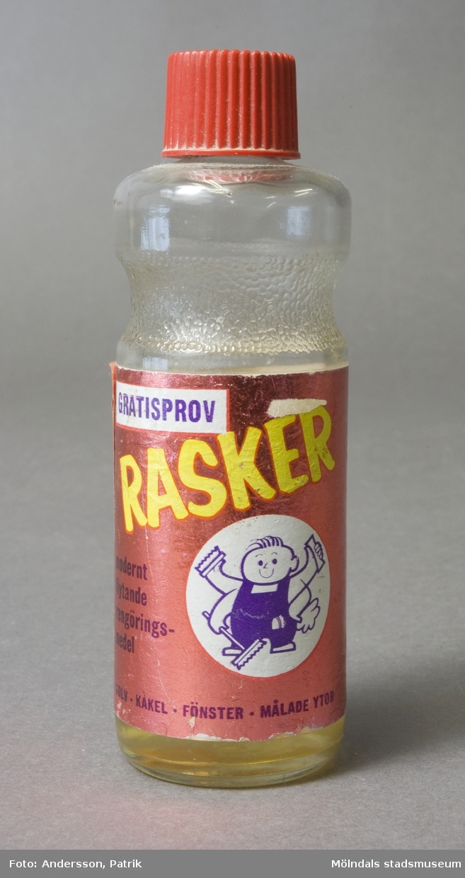 Glasflaska med skruvkork. Påklistrad etikett med texten; "Gratisprov - Rasker - modernt flytande rengöringsmedel". Bruksanvisning och tips står även på etikettens baksida. En del av innehållet är kvar i flaskan. 
