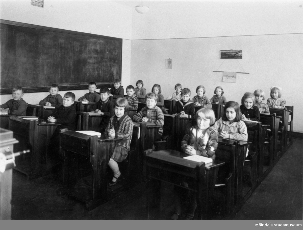 Elever sittande i sina bänkar med knäppta händer på Kvarnbyskolan i Mölndal ca 1930.