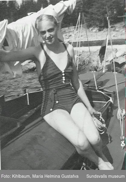 Kvinna i baddräkt sitter på en segelbåt.