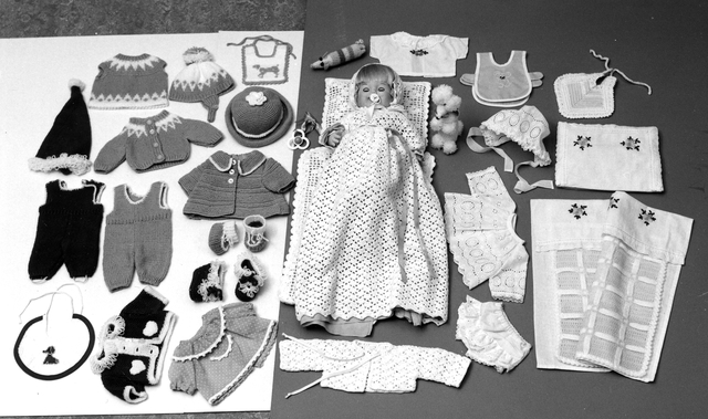 Docka, som ursprungligen lämnats in av bud från anonym givare
till "Posttomten" på Skansen omkring 1976. Handarbetade kläder, som
hör till dockan: Röd sitickad dräkt (sparkbyxor,kofta, mössa och
sockor); turkos stickad kappa, hatt och sockor; ljusblå och vit
stickad sparkbyxa, kofta,klänning och mössa; klänning, byxa och hätta
i vit brodyr; blå klänning med vita prickar; vit virkad dopklänning
fodrad med blått tyg med tillhörande hätta och kofta; skjorta med
broderad blå blomma, tre hadlappar och ett förkläde; virkat
paradtäcke med kudde; virkad filt i gult och vitt, lakan och örngott
med broderade gula blommor; två nappflaskor med virkade höljen i form
av en vit pudel och randigt fantasidjur.