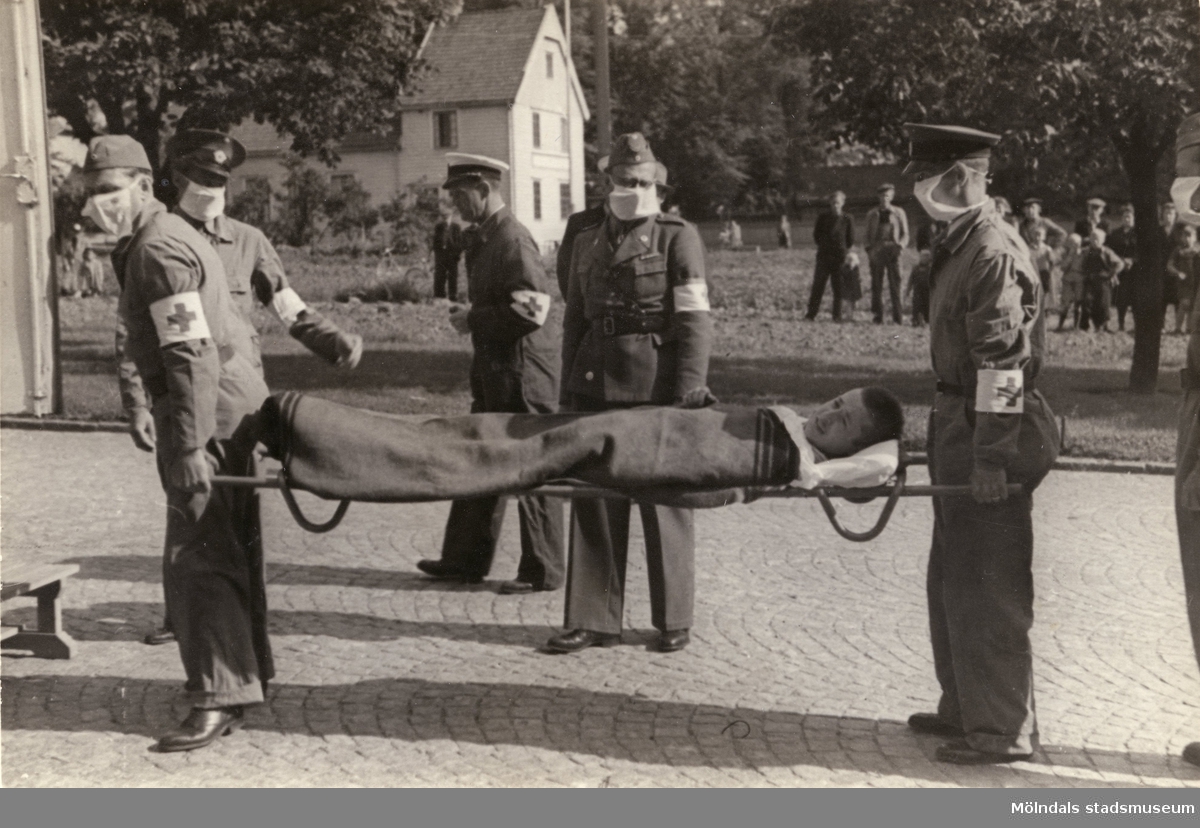 "Karantänsförläggning" på Kvarnbyskolan för överlevande från koncentrationsläger i Tyskland och Polen 1945.  
Skolan fungerade under denna sommar som beredsskapssjukhus.

Patient bärs in i förläggningen på bår av Röda Kors-arbetare.