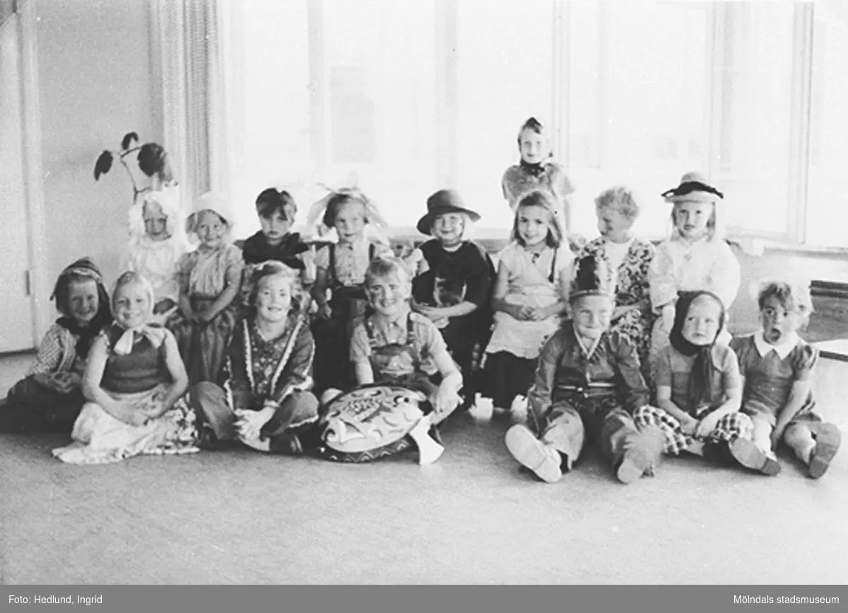 Utklädda barn vid en förskola i Guldheden, Göteborg, som sitter på golvet och tittar in i kameran. Bilden är tagen på sent 1940-tal.