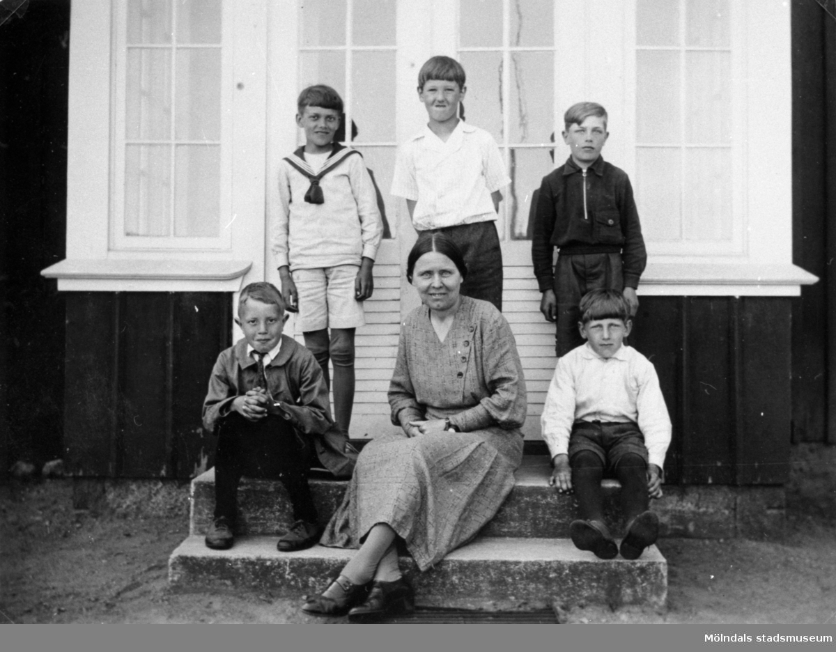 Fem pojkar poserar tillsammans med Valdeborg Johansson som sitter i mitten, våren 1934. Hon är med sina elever utanför skolan. Text på fotots baksida: "På trappan till 'Högskolan'". Samma elever som på bild 1992_0006, 0008. Ur Valdeborg Johanssons fotoalbum.