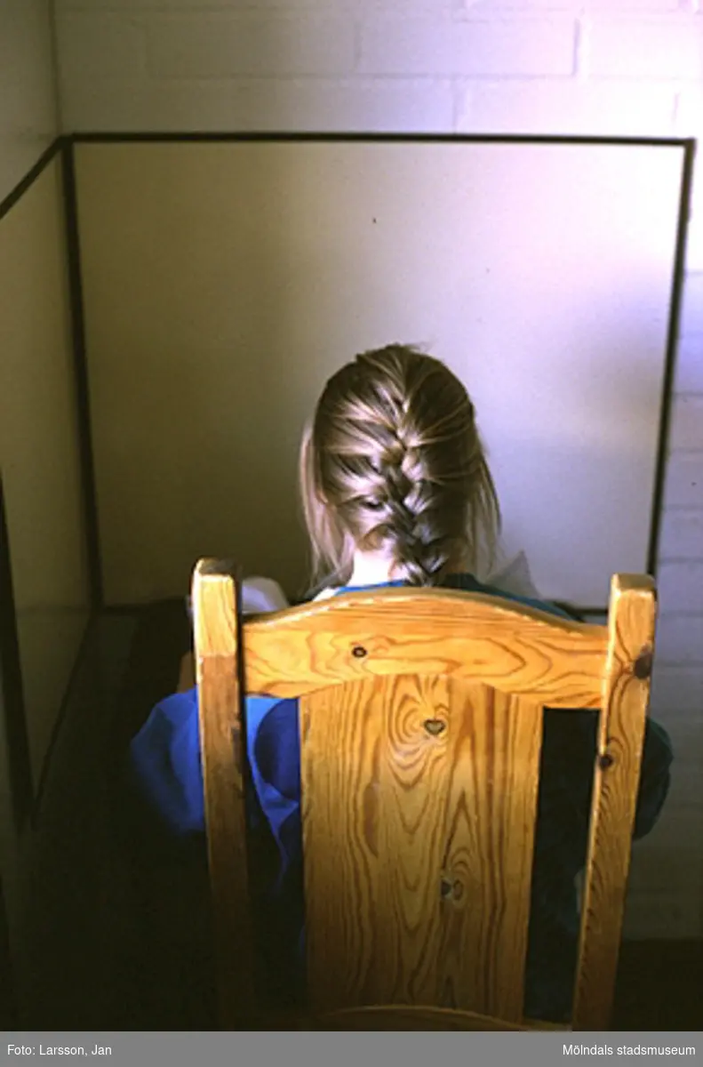 En kvinna med fläta sitter på en trästol framför en tegelvägg, troligen på Sagåsen 1980-tal.