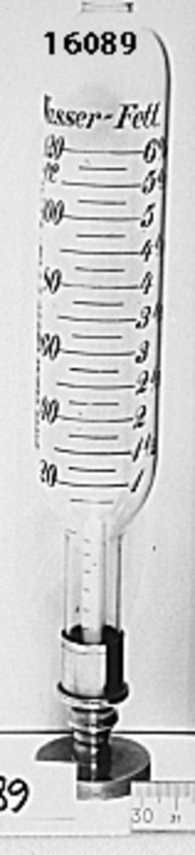 Lactoscop mjölkprovare. Cylindrisk glasbehållare, Prof. Feser. Graderad i två kolumner: Wasser 20-120  cc - Fett 1-6% i svart skrift. I glasbehållarens nederdel metallskruv i vilken en graderad glasstav är fästad. Denna del går att skruva bort från behållaren. Metallskoning i glasbehållarens nedre del, öppen i ovandelen.