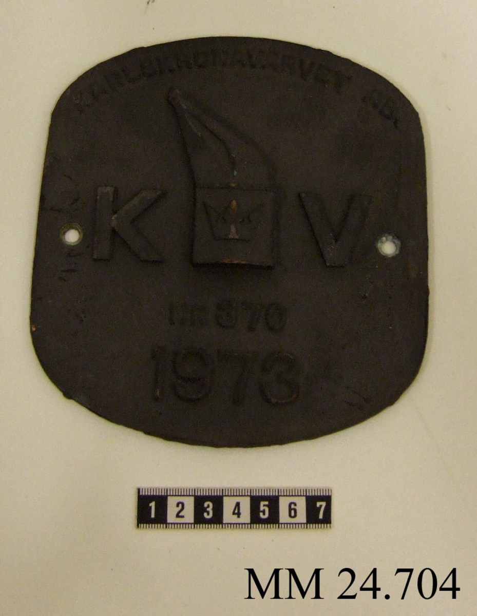 Metallskylt med inskription i relief. Texten på skylten lyder: Karlskronavarvet AB KV NR 370 1973. I mitten, dvs. texten KV, utformad som Karlskronavarvets logotype. Hål borrat i varje långsida.