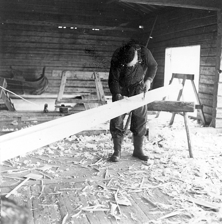 Neg nr 34. Johan Larsson justerar kölen med en yxa. kölen ligger på kant över båtbockarna. Foto 6.8 (1962).