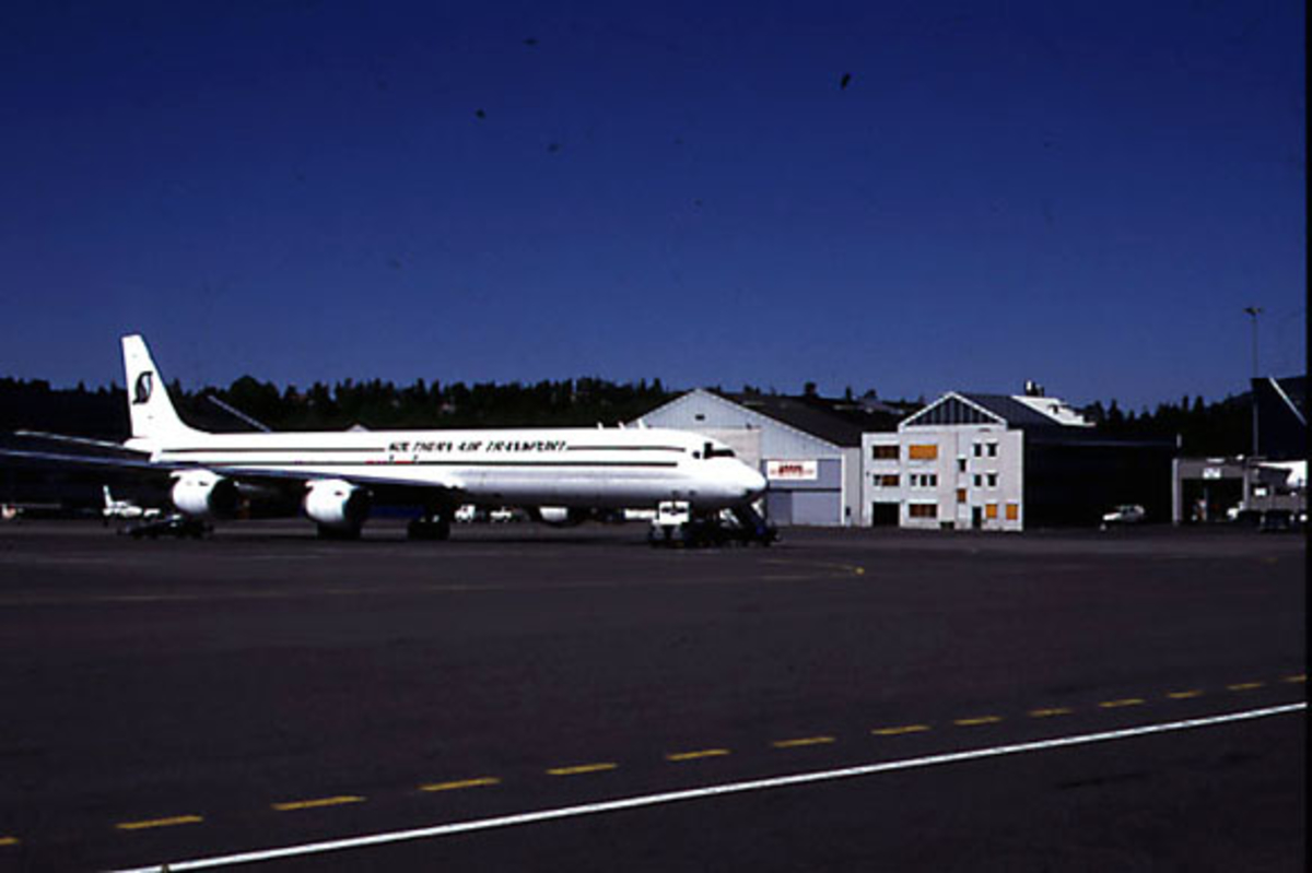 Lufthavn, 1 fly på bakken, DC.8 - 73 N-874SJ fra Southern Air Transport USA. Flyplassbygninger og andre fly bak.
