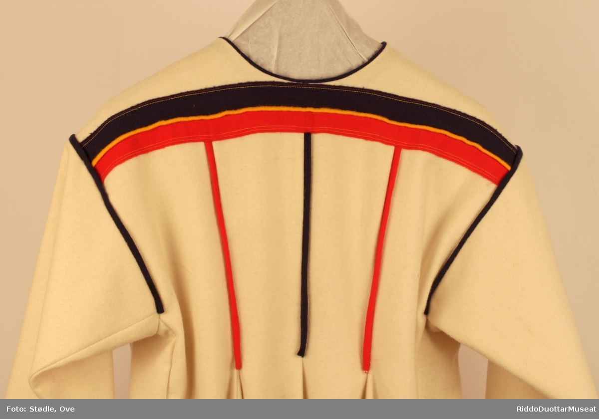 Kofta har påsydd dekorklede i rødt, blått og gult på bryst, skuldre, holbi, rygg og ermer. På fremre holbikant er det to tagger av gult klede som skiller seg ut .