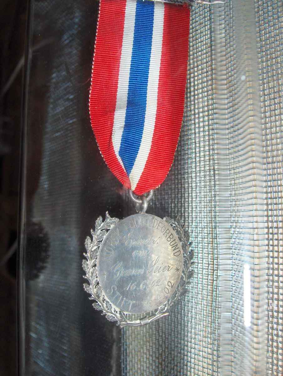 Gravert medalje med norsk sløyfe.
