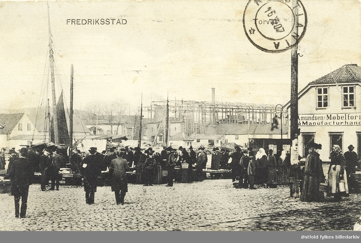 Torget i Fredrikstad fra prospektkort stemplet 1907.
Utsikt over mot Kråkerøy.
Amundsens Møbelforretning og Manufakturhandel ligger i enden av torget.

Fiskebasarene ble bygd i 1890 og ligger utenfor venstre bildekant. FMV i bakgrunnen med et rammeverk rundt stedet der båtene ble bygd.