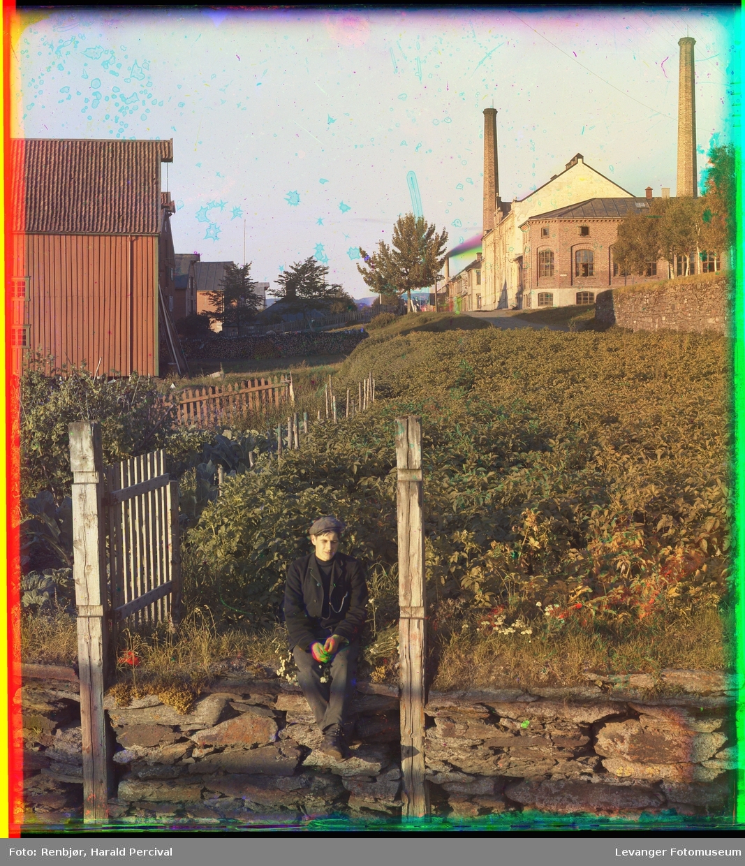 Ung mann sittende ved Levangersundet, med brygge, melkefabrikken og kirkegårdsmuren i bakgrunnen.