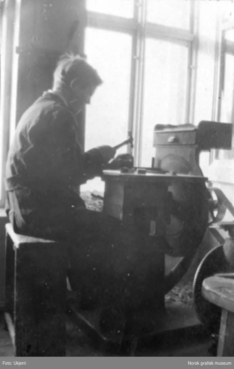 En mann sitter ved en pult og fester klisjeer på treklosser ved bruk av hammer og spiker. Dreyers Reproduktionsanstalt.
Albumtekst:
"Montøren (Boysen) set fra hans daarlige side"