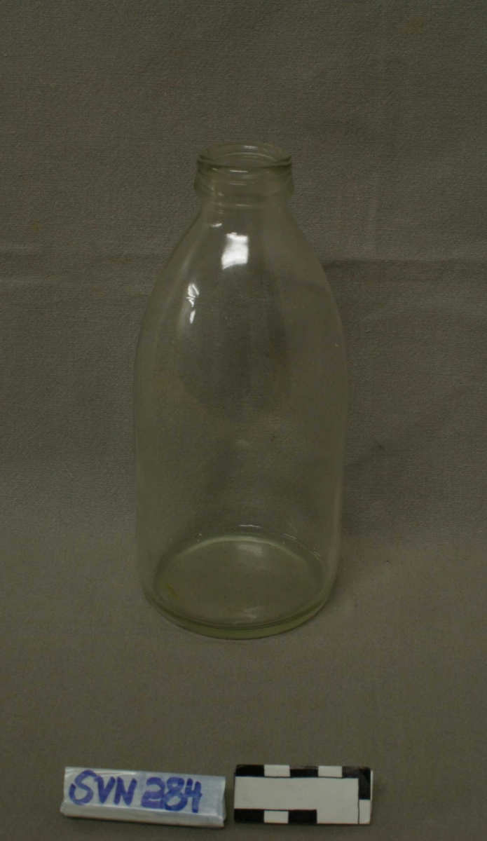 Flaske med bred kropp og kort, bred hals. I gjennomsiktig glass.