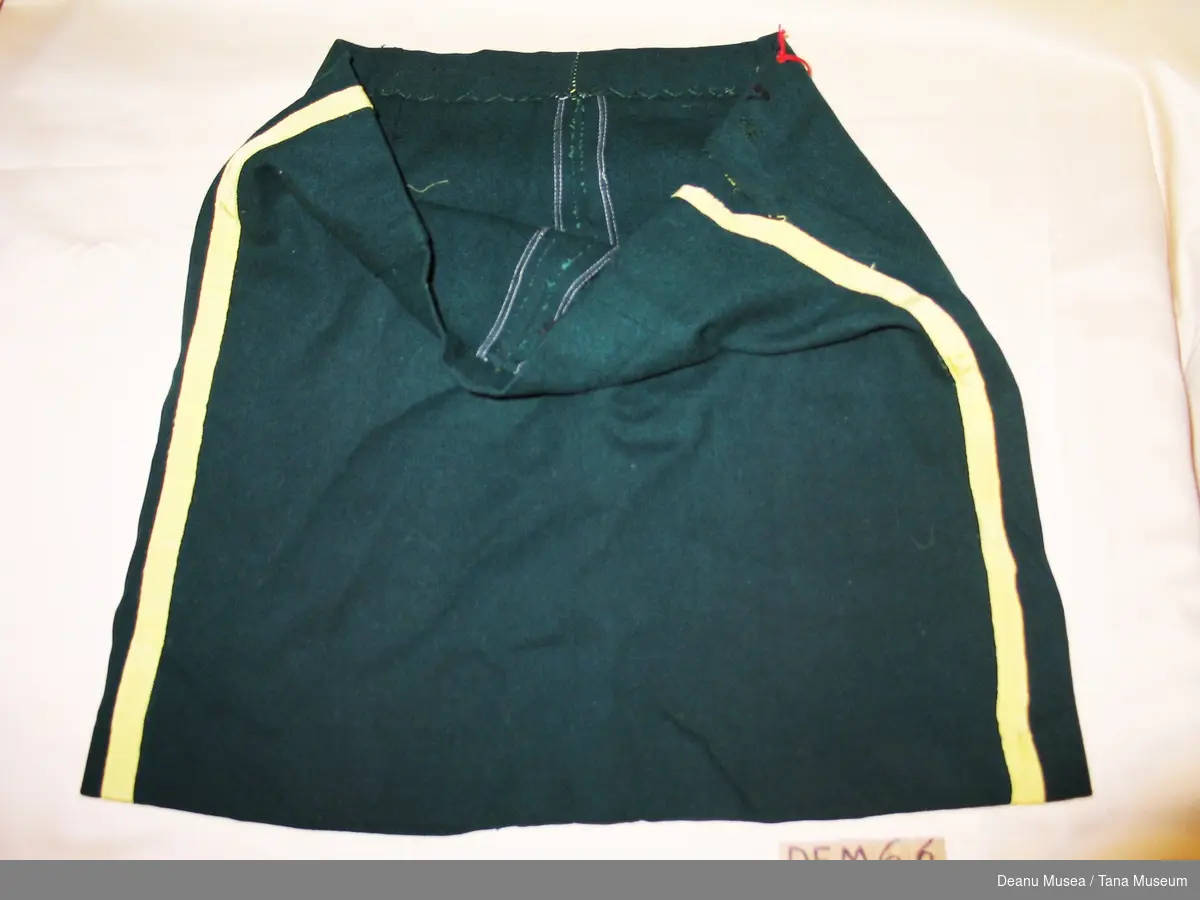 Skjørtet er sydd av mørkegrønt klede i ull med påsydde gule bånd i silke . 