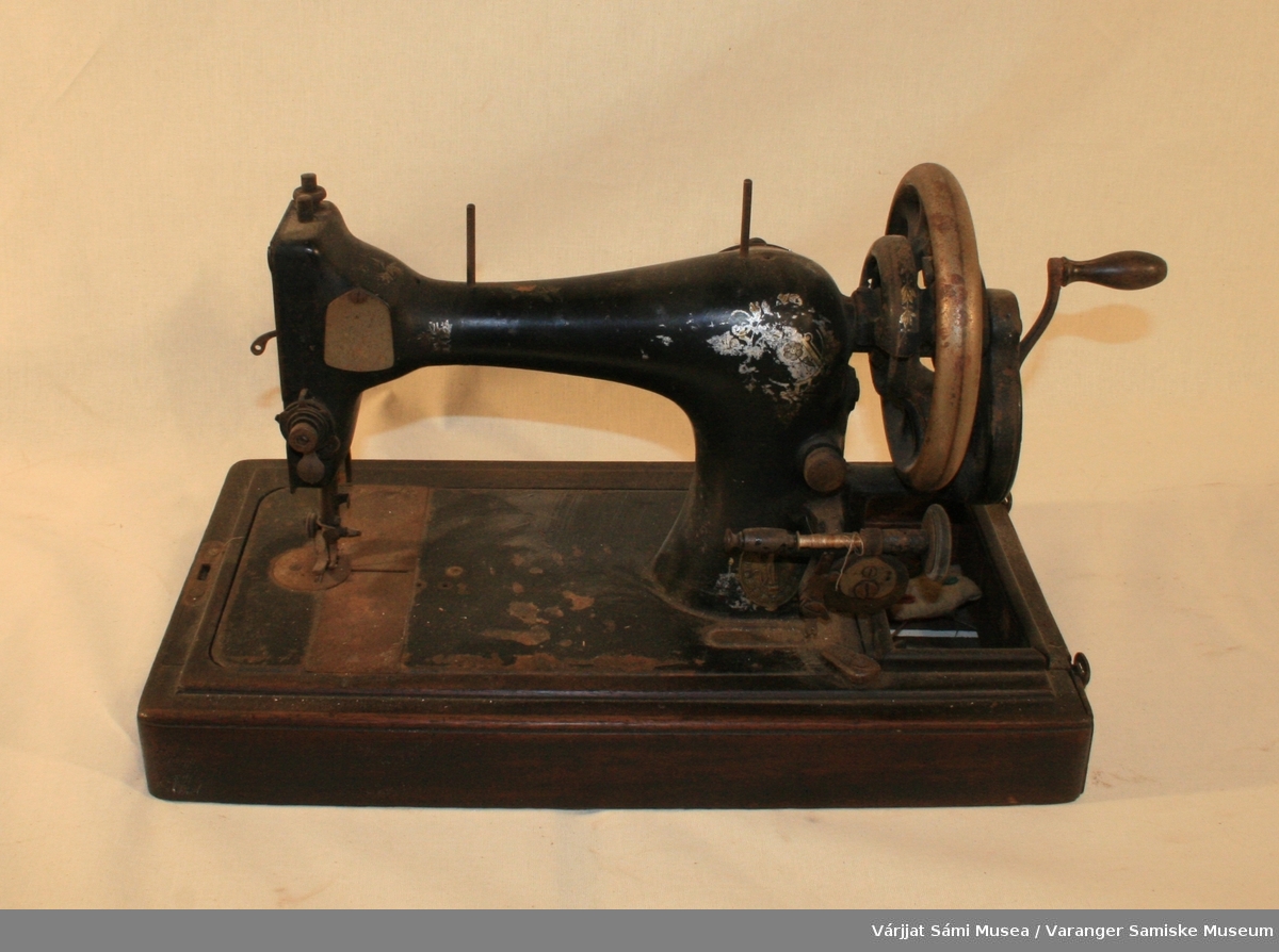 Hånddrevet symaskin fra Singer, selve maskinen er av sortmalt metall mens foten / sokkelen er av brunt tre.