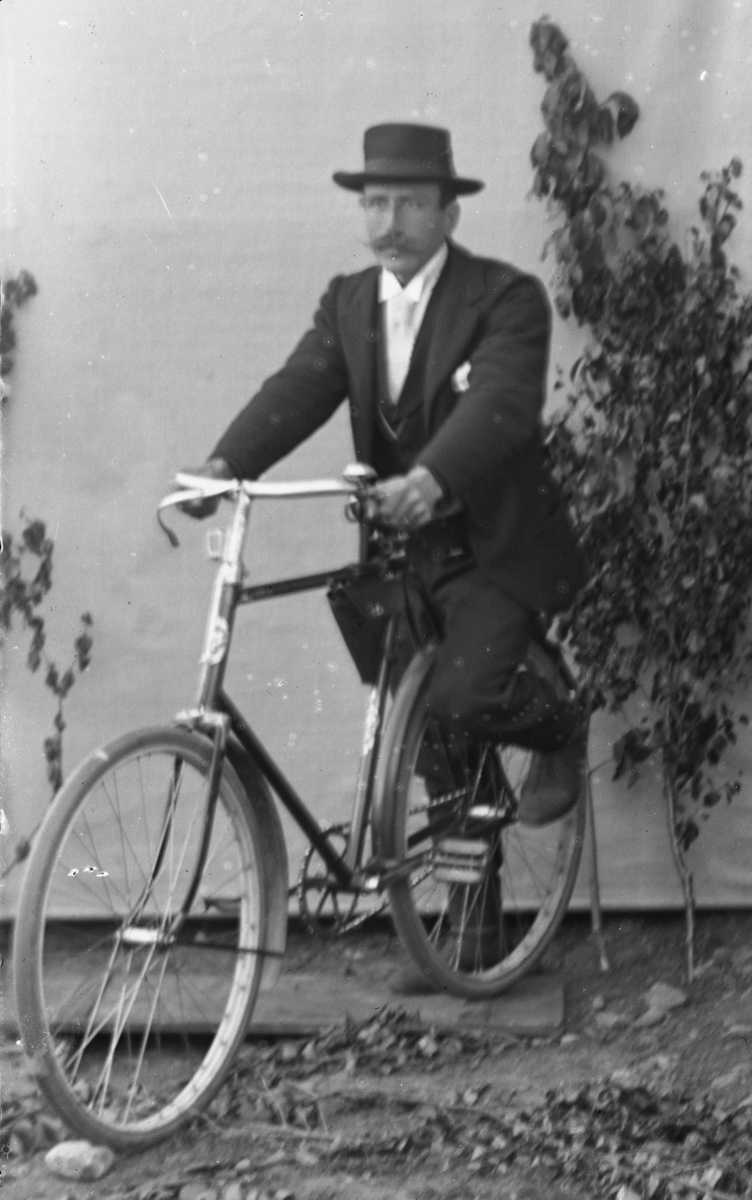 Dresskledd mann på sykkel med lerretbakgrunn.