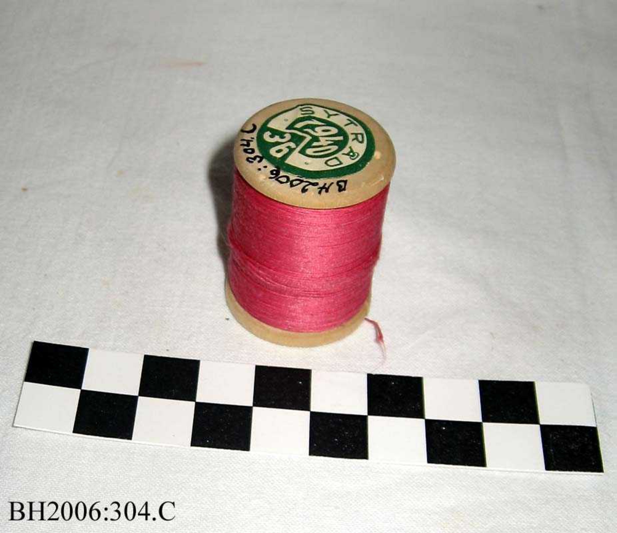 Trådsnelle med rosa tråd, og kjerne av tre og etikett i hver ende.