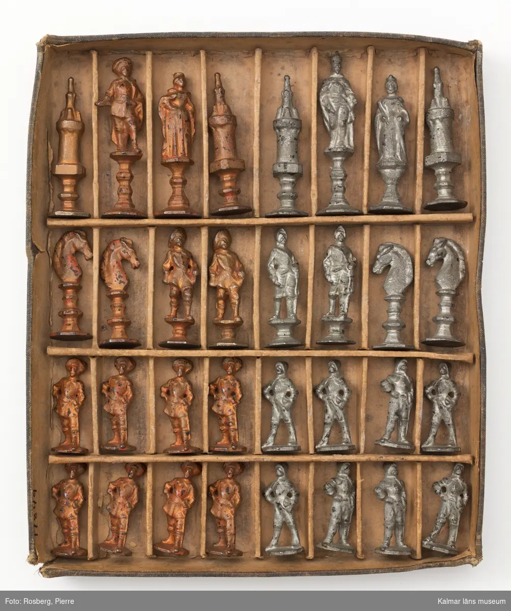 KLM 17849 Schackspel, av gjutjärn. 32 pjäser i ask av kartong. Figurernas höjd varierar mellan 4,5-8,1 cm. Figurerna bär 1600-tals dräkter. Hälften av pjäserna är silverfärgade, andra hälften är rödbronsfärgade. Tillverkade vid Fredrikströms bruk, gjuteriet, enligt uppgift av givaren. Datering, möjligen tillverkade redan på 1850-talet.
